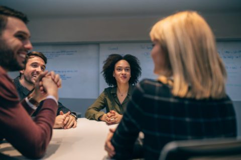 People sitting around a table, pleasantly speaking with one another, and respectfully listening to what each other says.